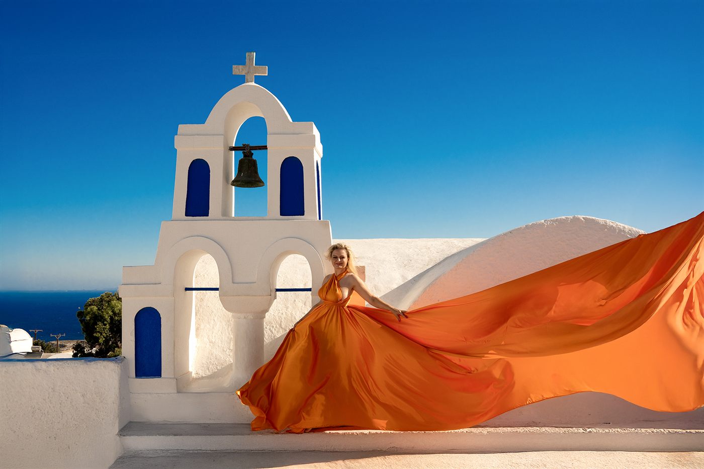 Agnieszka Wójtowicz w pomarańczowej sukni przy dzwonnicy na Santorini - nowy kierunek zawodowy
